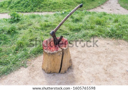 Axe of executioner from middle Ages. Beheading on medieval festival. Victim's blood on wooden stump. Bloody wood block at place of execution of defendant.