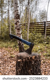 An axe will be stuck into a wooden log. Harvesting firewood for the winter season. Logging on the background of the forest. Lumber, wood-cutting tools.