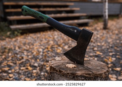 An axe will be stuck into a wooden log. Harvesting firewood for the winter season. Logging on the background of a country house. Lumber, wood-cutting tools.