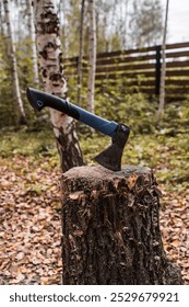 An axe will be stuck into a wooden log. Harvesting firewood for the winter season. Logging on the background of the forest. Lumber, wood-cutting tools.