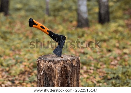 An axe will be stuck into a wooden log. Harvesting firewood for the winter season. Logging on the background of the forest. Lumber, wood-cutting tools.