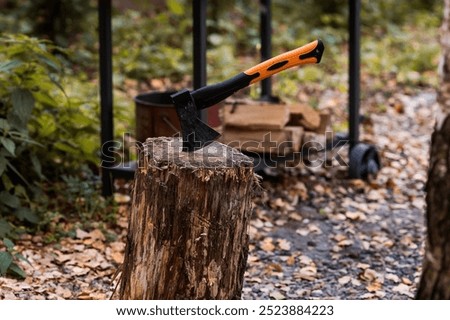 An axe will be stuck into a wooden log. Harvesting firewood for the winter season. Logging on the background of the forest. Lumber, wood-cutting tools.