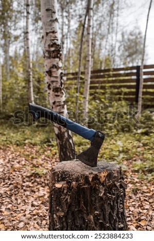 An axe will be stuck into a wooden log. Harvesting firewood for the winter season. Logging on the background of the forest. Lumber, wood-cutting tools.