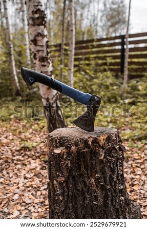 An axe will be stuck into a wooden log. Harvesting firewood for the winter season. Logging on the background of the forest. Lumber, wood-cutting tools.