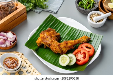 Ayam bakar or roasted chicken on banana leaf shoot at a rustic wooden background. Ayam bakar is a indonesian dish. Ayam bakar literally means "roasted chicken", in the smoky burning process.