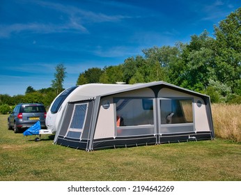 Aylesbury, UK - Jul 9 2022: Pitched In A Grassy Field, A White Caravan With Full Awning And Car On A Sunny Day With A Blue Sky In Summer.