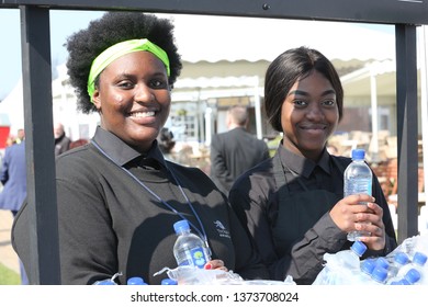 AYR RACECOURSE, AYRSHIRE, SCOTLAND, UK : 12 APRIL 2019 : Two Attractive Black Girls Smiling And Having Fun As They Act As Water Attendants During The Scottish Grand National Meeting At Ayr