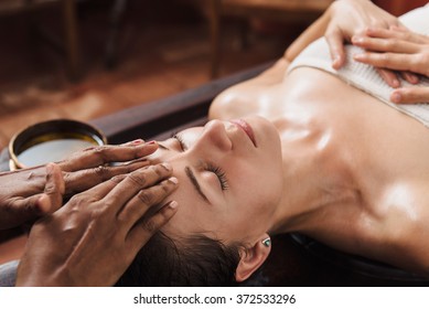 Ayurvedic face massage with oil on the wooden table in traditional style made by asian women. 