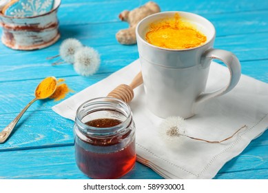 Ayurvedic golden milk with turmeric powder, honey and ginger in blue wooden background. flu remedy, cure for sore throat, detox, healthy drink. close up and selective focus