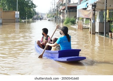 Ayutthaya Thailand-October 1,2021:Lady rowing along flooded road. Heavy rain caused water high levels in street. It's nature disaster. Building background. She and son wear face masks for safe travel.