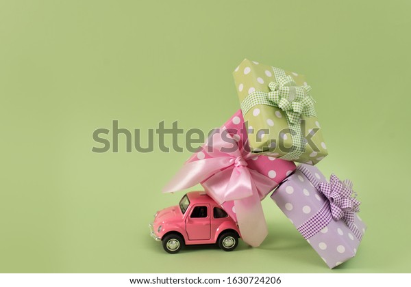 Azov, Russia January 29, 2020.\
Pink toy car delivers a gift box on green background. February 14\
postcard, Valentine\'s Day. March 8, international women\'s\
day