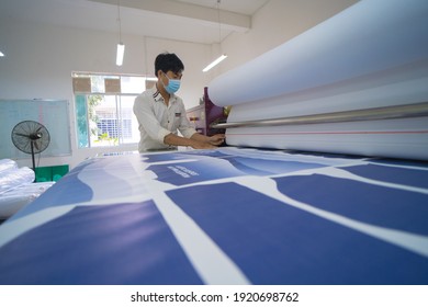 Ba Ria, VIETNAM -  19 FEB 2021: Young asian male worker technician wearing medical mask make object on sublimation heat press machine in digital printshop office. Sublimation concept.