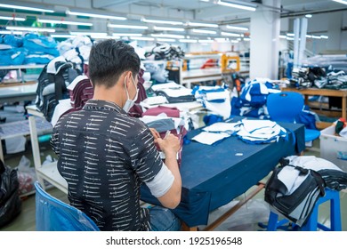 Ba Ria, VIETNAM - 26 FEB 2021: Man wearing medical mask writting number on fabric after finished cut. Textile cloth factory working process tailoring workers equipment