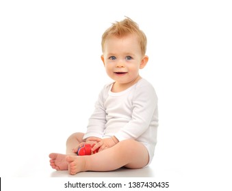 Baby 11 months in a white bodysuit sitting on a white background and holding a toy
