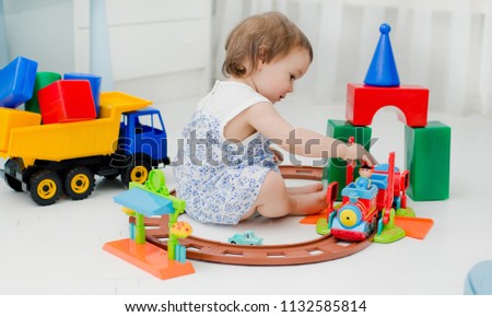 baby 2 years old playing with lots of colorful plastic toys indoors. A little girl playing on the floor in the train and the railway with a tunnel