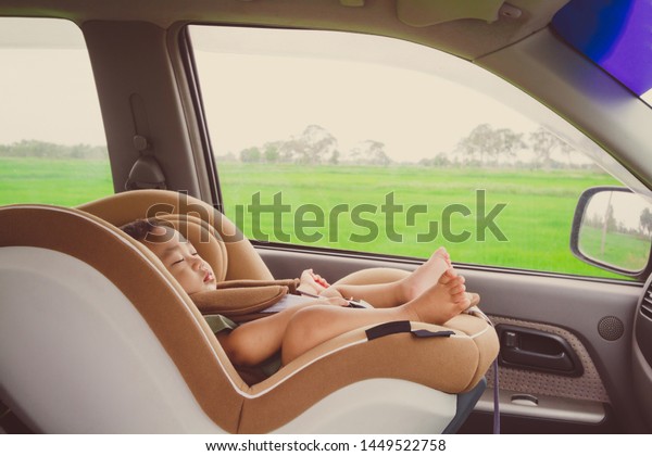 Baby 7 months old sleeping in\
comfortable car seat on rural road with rice field\
background.