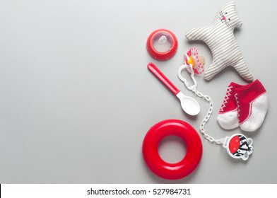 Baby Accessories Background: Socks, Soother, Nipple, Spoon And Toys Over Grey Background With Copy Space; Top View, Flat Lay.