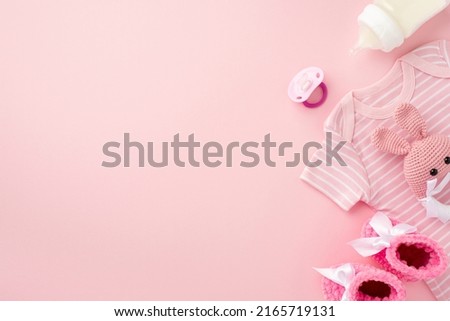 Baby accessories concept. Top view photo of pink infant clothes bodysuit booties baby's dummy bottle and knitted bunny rattle toy on isolated pastel pink background with empty space