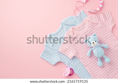 Baby accessories concept. Top view photo of pink and blue bodysuits baby's dummy chain and knitted teddy-bear toy on isolated pastel pink background