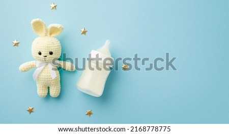 Baby accessories concept. Top view photo of knitted bunny toy milk bottle and gold stars on isolated pastel blue background with copyspace