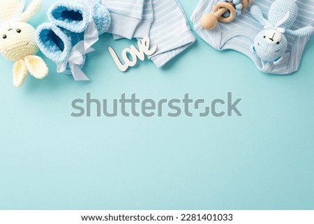 Baby accessories concept. Top view photo of infant clothes blue shirt pants inscription love knitted booties wooden rattle teddy bear and bunny toys on isolated pastel blue background with empty space