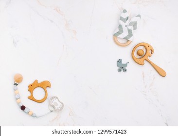 Baby accessories (soother, wooden toys, beanbag and teethers) on light marble background with blank space for text. Top view, flat lay.