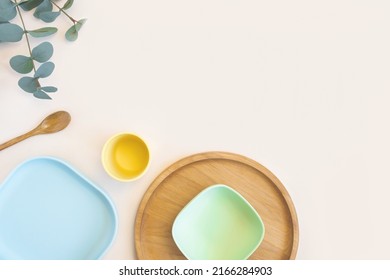 Baby Accessories And Tableware For Food On Beige Background. First Feeding For Kids Concept. Flat Lay, Top View, Space For Text. Silicone Dishware, Bib, Cup On Neutral Backdrop. Serving Baby Food.