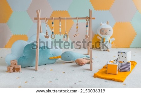 Baby activity gym play toys hanging from wooden arch on playmat in nursery or playroom. Home decoration children objects with learning cubes, plush cloud toy, whale decor banner