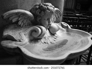 Baby angel over holy water stoup in church. Aged photo. Black and white.