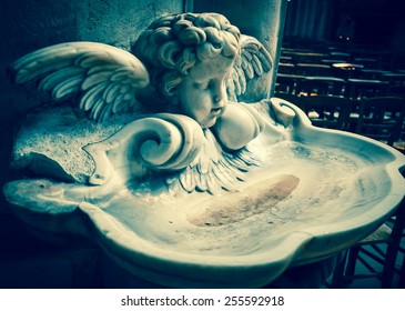 Baby angel over holy water stoup in church. Aged photo. 