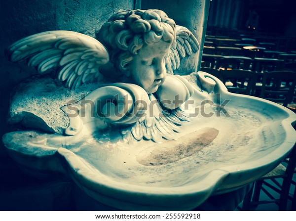Baby\
angel over holy water stoup in church. Aged photo.\
