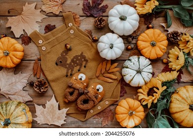 Baby Autumn Wear Clothes With Pumpkins And Leaves On Brown Background. Top View. Cute Warm Kid Autumn Bodysuit And Booties. Autumn Baby Shower