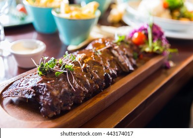 Baby Back Ribs With Sauce Served On A Wooden Plate With Side Dishes And Sauces
