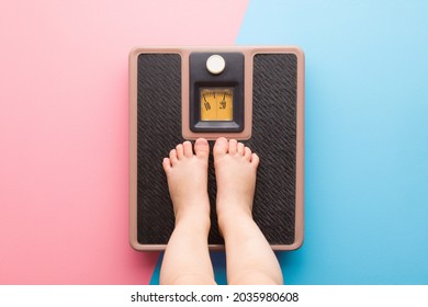 Baby barefoot standing on weight scales on light pink blue floor background. Pastel color. Closeup. Care about body. Children weight control concept.