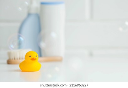 Baby bath accessories. Child care. Miniature yellow rubber duckling for bathing with a brush and shampoo bottles. Soap bubbles, bath foam. - Shutterstock ID 2116968227
