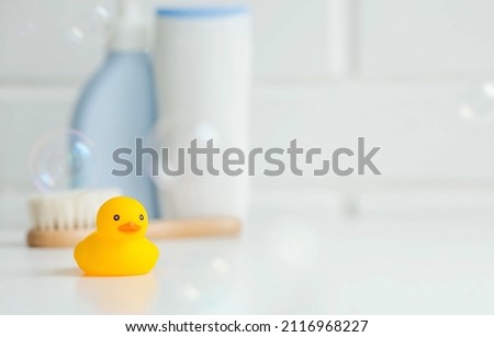 Baby bath accessories. Child care. Miniature yellow rubber duckling for bathing with a brush and shampoo bottles. Soap bubbles, bath foam.