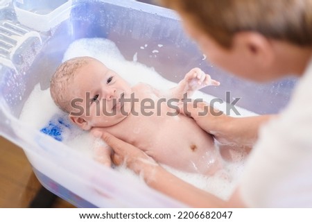 Baby bath time. Close-up detail view of mother bathing cute little peaceful baby in tub with water and bubbles lather	