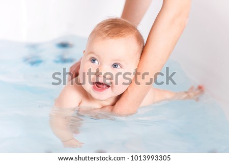 Baby bathing. Mother's hands holding a baby swimming in bathroom