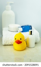 Baby Bathing Products, Baby Care, Yellow Rubber Duck For Playing In The Bath. Children's Cosmetics, Toys And A White Towel On The Table On A White Background. Selective Focus.