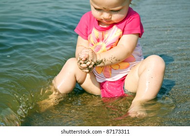 Baby in bathing suit playing with sand in beach waves