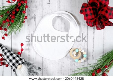 Baby bib product mockup. Christmas farmhouse theme SVG craft product mockup styled with gift with buffalo plaid bow and farmhouse style gnomes against a white wood background.
