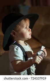 A Baby In A Black Broad-brimmed Hat Holds A Magnifying Glass And A Playing Card In Her Hands And Stands In Profile