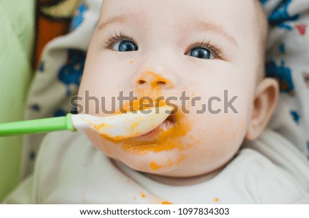 baby with blue eyes eating pumpkin puree all smeared and drenched