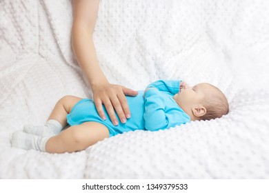 The Baby In Blue Pajamas Is Sleeping While Mom Pats Him, Mom Takes Care Of Her Son, Baby In Blue Pajamas Lying On A White Blanket, Mother's Hand Gently Strokes The Baby's Tummy