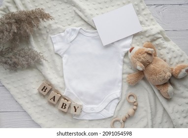 Baby bodysuit and card mockup on soft blanket, toy bear, wooden blocks, pampas grass, neutral bohemian pregnancy announcement background.