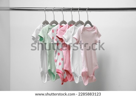 Baby bodysuits hanging on rack near white wall
