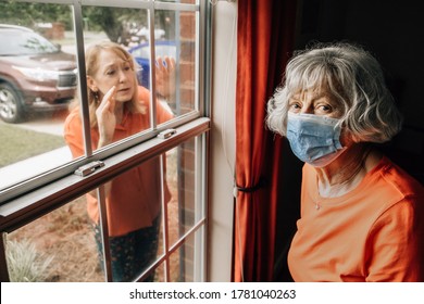 A Baby Boomer Daughter Visiting Her Elderly Shut-in Mother In Her 80's During Quarantine From Covid-19 Coronavirus Through A Window As To Not Catch This Contagious Disease