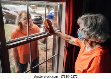 A baby boomer daughter visiting her elderly shut-in mother in her 80's during quarantine from covid-19 coronavirus through a window as to not catch this contagious disease