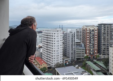 Baby Boomer Retired Man Looks At View Of Apartment Buildings From Balcony In Auckland, New Zealand, NZ