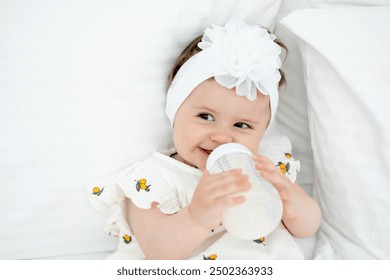 a baby with a bottle of milk or formula in his hands in a bright bedroom, a space for text, a baby food concept, a small child sucking a pacifier with a bottle. - Powered by Shutterstock